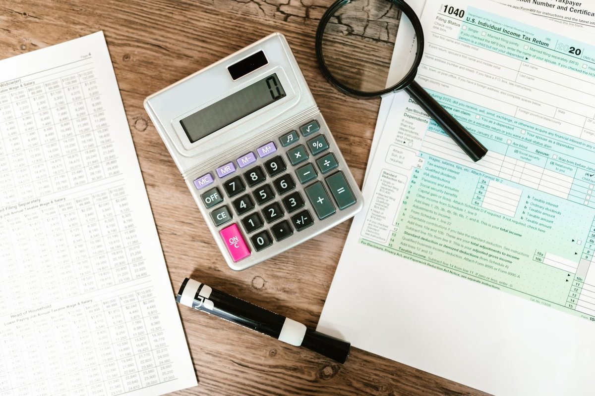Calculator, magnifying glass, and financial forms arranged on a wooden desk
